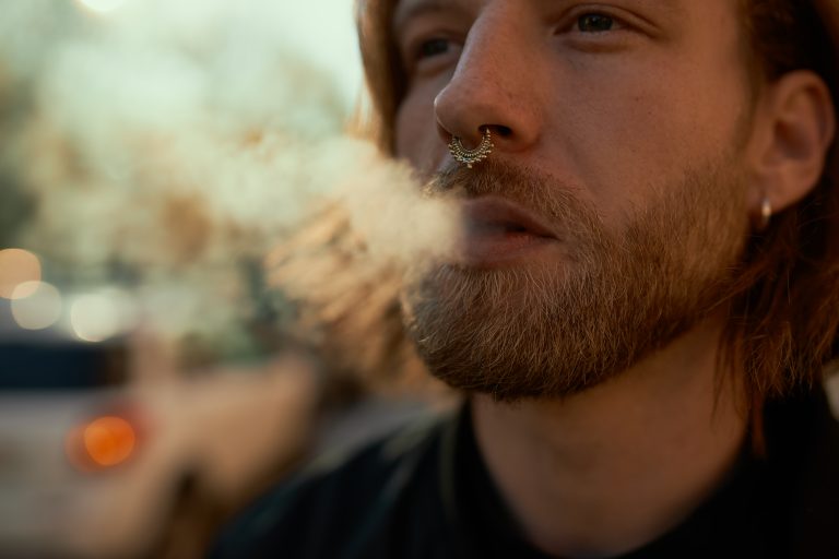 cropped-shot-handsome-stylish-young-bearded-male-vaping-electronic-cigarette-outdoors-close-attractive-guy-with-nose-ring-puffing-smoke-while-walking-city-street-sunny-summer-day-scaled